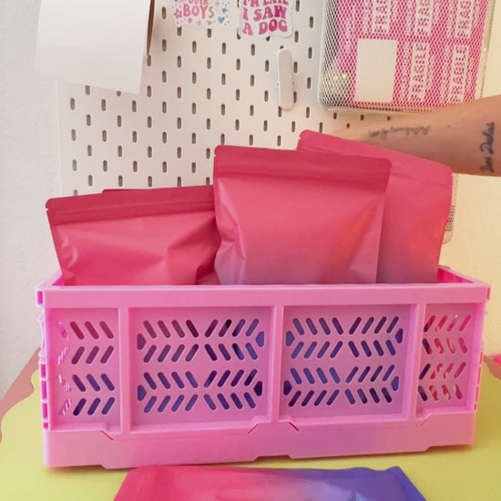 Video revealing colorful cartoon mystery gift bags being packed into a bright pink mini plastic storage crate.