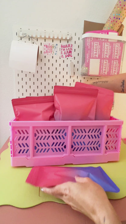 Video revealing colorful cartoon mystery gift bags being packed into a bright pink mini plastic storage crate.